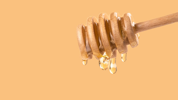 有机液体蜂蜜滴从蜂蜜勺在一个轻的背景。健康食品的概念。金色的蜂蜜滴倒和流动从木制勺子图片下载