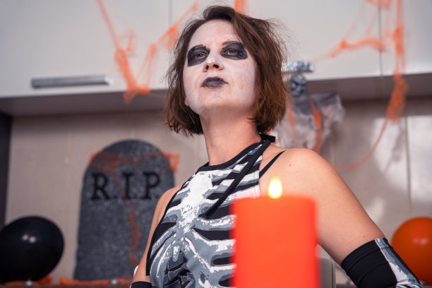 一幅年轻狂野女人的肖像，画着令人毛骨悚然的妆容，红色的恶魔般的眼睛和凝视，穿着主题派对或戏剧表演的服装，正面以蜡烛为背景图片下载