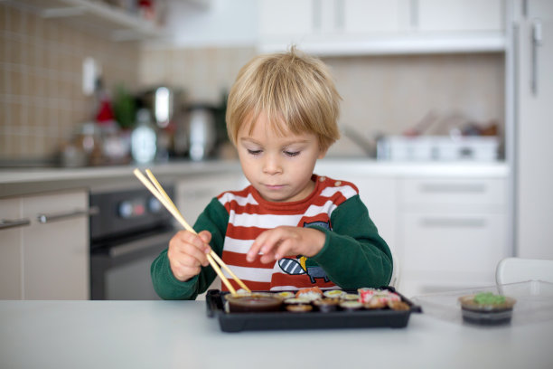 可爱的金发小孩在家吃寿司卷。快乐男孩可以吃寿司了图片下载
