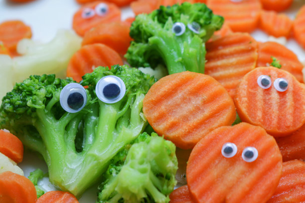 全帧图像的冷冻混合蔬菜堆在一个白色的盘子上，瞪大的眼睛添加了皱纹切胡萝卜片和花椰菜和花椰菜的小花，儿童健康饮食，幽默的概念图片下载
