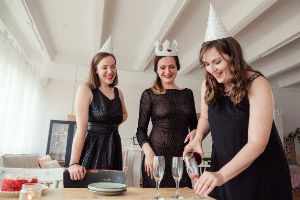 和围坐在桌子旁的朋友们一起，一个人把白葡萄酒从瓶子里倒进玻璃杯里。一群在餐馆吃东西喝饮料的年轻人。图片下载