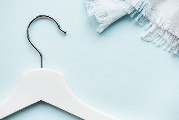 白色羊毛围巾的碎片和浅蓝色背景上带有金属钩的白色木制衣架图片下载
