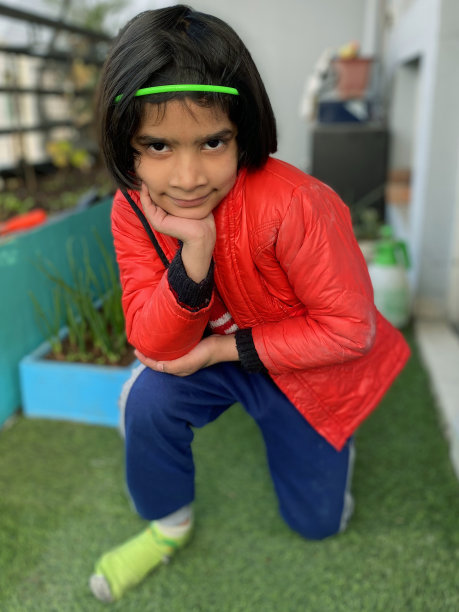 特写镜头:年轻的印度女孩跪在种植着红绿珊瑚生菜叶子的菜圃旁边，洛洛·比昂达(浅绿色)，洛洛·罗索(红色)，鸽子防鸟网，看着相机图片下载