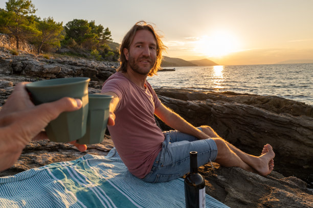 日落时分，一对年轻夫妇在海岸线上喝酒图片下载
