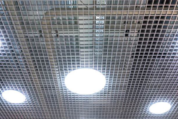 商业建筑天花板上的三个圆形LED照明灯。网状吊顶为购物中心或办公楼的内部创造了一种美丽的建筑外观。图片下载