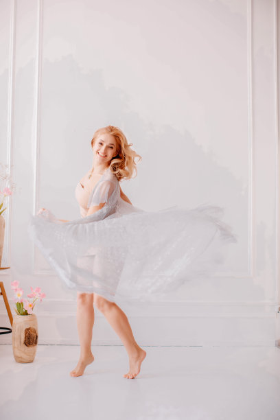 那女孩穿着白裙子在白墙的背景下旋转。图片下载