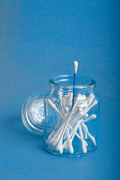 打开装有棉签的玻璃药瓶，蓝色背景上有毗邻的盖子图片下载