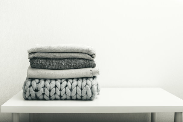 白色的桌子上放着一叠灰色的毛织毛毯图片下载