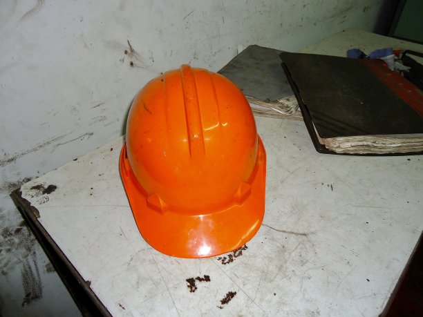 白色的桌子上放着一本旧书和一顶橙色的头盔图片下载