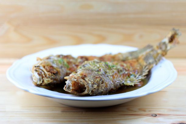 泰国巨大的丝瓜鱼和大蒜油炸和甜辣酱在白色盘子松木桌上。用甜辣椒油炸的鱼。泰国菜辣酱炸鱼。泰国风格的食物。图片下载