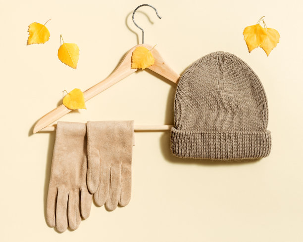 米色针织帽和绒面手套挂在衣架上装饰黄色的秋叶。秋季时尚概念图片下载