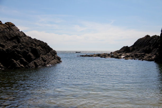 美丽的风景照片海岸入口周围的岩石露头与一艘船在一个平静的海洋中心在夏天的一天。图片下载