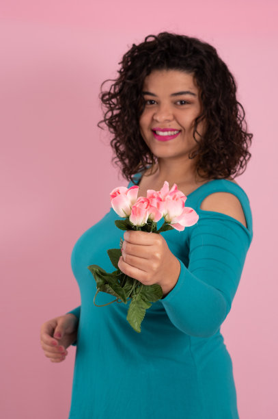 一名年轻女子手持粉红色背景上的一束鲜花图片下载
