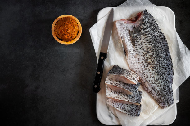 新鲜的鲈鱼片放在大理石砧板上，木碗里放辣椒酱。顶视图在黑色背景与复制空间。图片下载