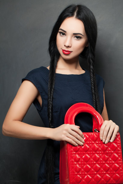 时尚的照片，一个美丽优雅的年轻女子在一个漂亮的蓝色裙子拿着红色的手提包在灰色的背景图片下载