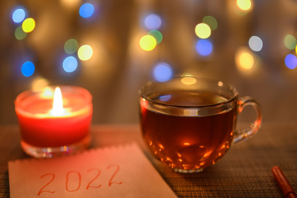 一本写着“2022”字样的笔记本和一支钢笔，背景是闪闪发光的新年花环。图片下载