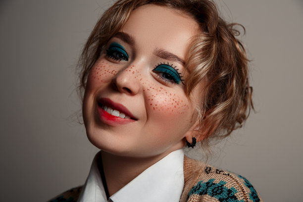 一个年轻漂亮的蓝眼睛女孩，穿着衬衫和夹克。脸上画着雀斑，脸上带着愉快的微笑。在一个灰色孤立的背景上。图片下载