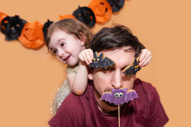 父亲和女儿在橘色的孤立背景下与姜饼蝙蝠曲奇嬉戏。图片下载