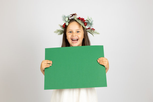 特写照片的笑女孩在圣诞节花环持有绿色的纸孤立在白色的背景图片下载