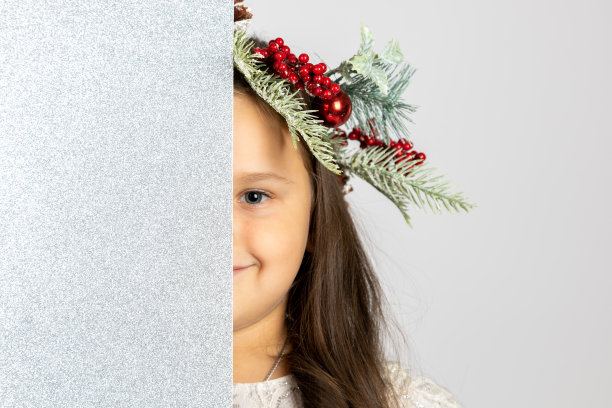 近距离的肖像微笑的美妙的女孩在圣诞树花环隐藏半脸背后的银色，闪亮的空白旗帜孤立在白色的背景图片下载