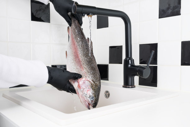 戴着黑色橡胶手套的手在流动的水中处理鱼图片下载