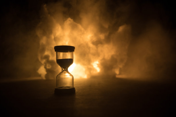 时间的概念。沙漏时钟的剪影和古老的老式木钟与箭和烟在黑暗的背景与热黄橙红蓝冷背灯，或复制空间的时间符号图片下载