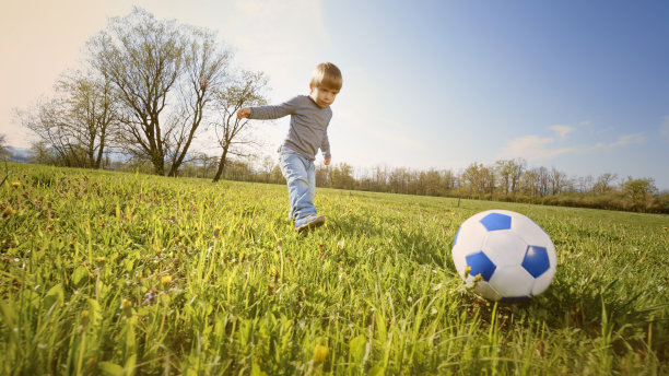 男孩在阳光明媚的草地上踢足球图片下载