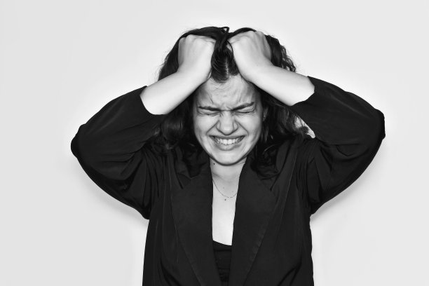 这是一个心情不好的年轻女人的肖像，她很生气，尖叫着，用手捋着头发，拉着自己，皱眉，闭上眼睛，露出牙齿，穿着黑色的商务夹克。图片下载