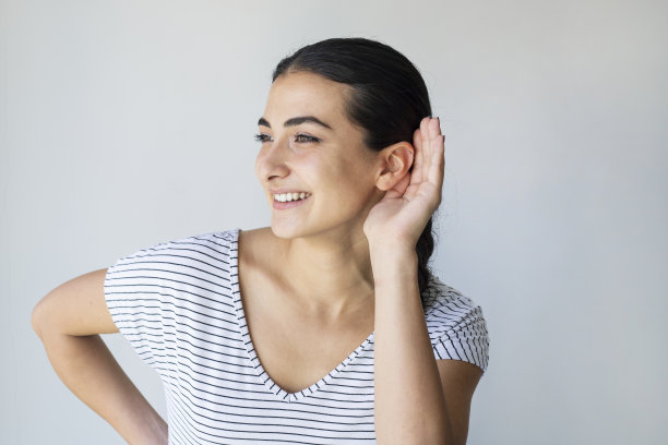 年轻女子在孤立的灰色背景下听东西，把手放在耳朵上图片下载