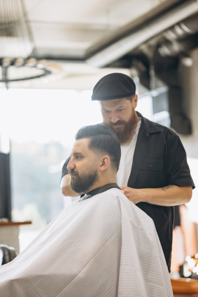 两个英俊的男人在理发店。时尚的红胡子理发师和客户在理发过程中。美容、保健和男性化妆品概念。图片下载
