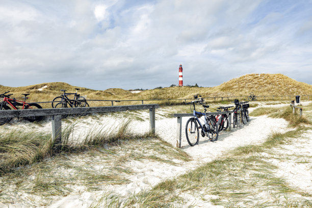 几辆不同的自行车靠在指定的自行车停放处的木架子上。背景是高大的红白条纹灯塔。图片下载