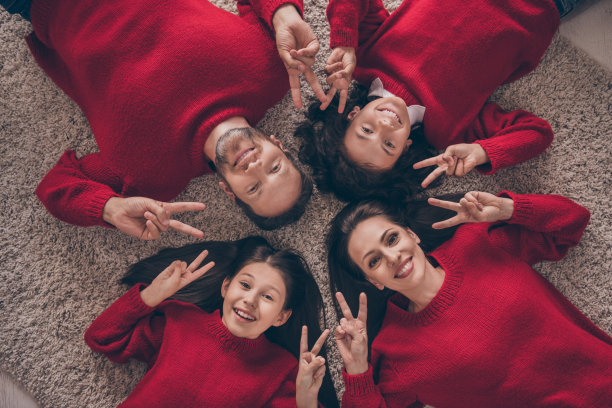 有趣的家庭照片躺在地毯上展示v-sign穿红色套头衫新年在家里图片下载