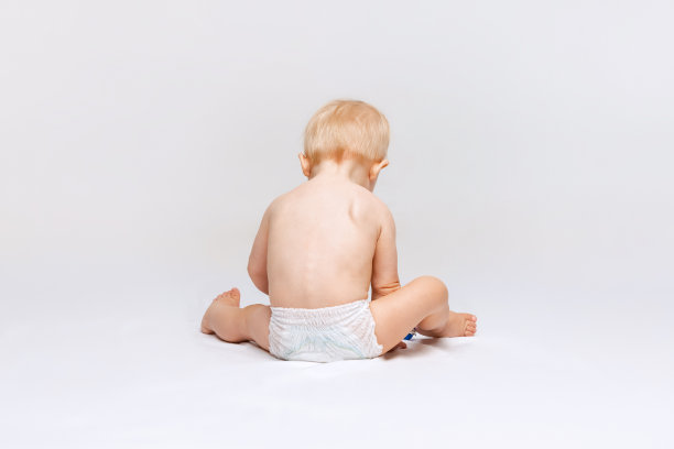 全身后视镜的小可爱的蹒跚学步的女孩，婴儿平静地坐在尿布和玩孤立的白色工作室背景。图片下载