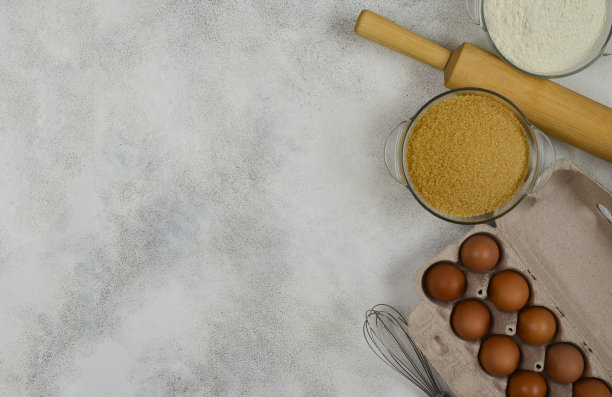 混凝土桌子上自制蛋糕的原料，环保纸板包装的农场鸡蛋，擀面棍，打蛋器，面粉和红糖图片下载