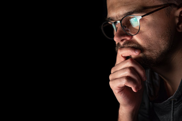 一个戴着眼镜的人在黑暗中看着电脑屏幕，拷贝空间。图片下载