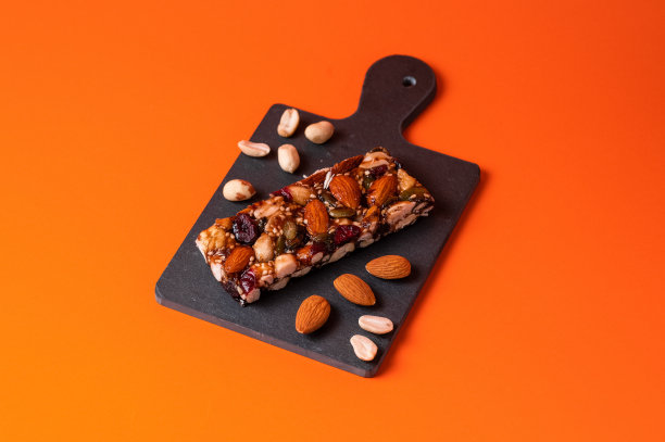 健康的零食，健身的生活方式和高纤维的饮食理念，格兰诺拉燕麦能量棒周围环绕着干果，榛子和杏仁在黑色的石头上与引人入胜的光线图片下载