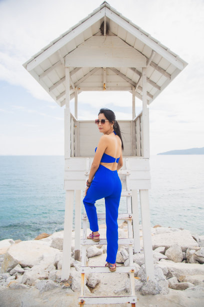 人像亚洲女子身穿蓝色西装，坐在白色警卫室前的大海和天空的背景。图片下载