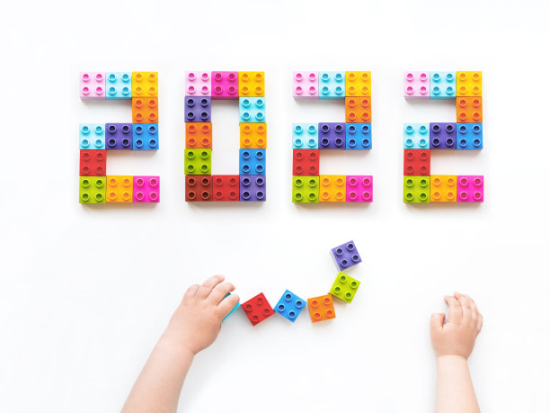 2022年新年。孩子正在玩彩色的构造函数块。孩子的手拿着白色背景的砖头玩具。教育玩具，平放，俯视图。图片下载
