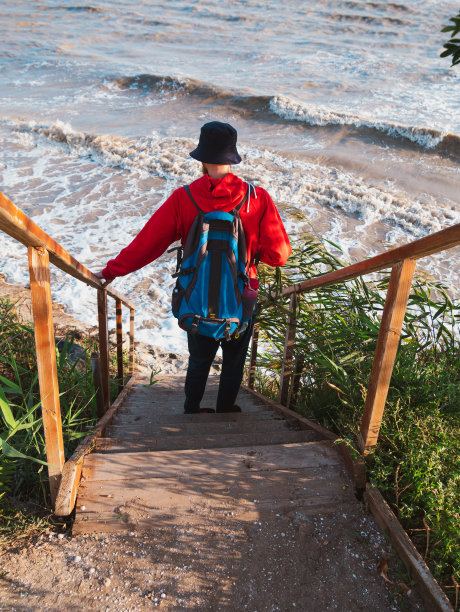 留着胡子的千禧一代男子穿着红色连帽衫背包秋天的海背景干芦苇真实的男性旅游生活方式的照片图片下载