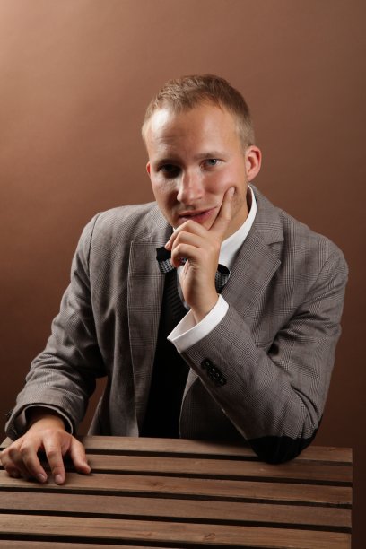 一位英俊、自信的商人，穿着西装，独自坐在棕色背景上，直视着镜头。一个成功企业的概念图片下载