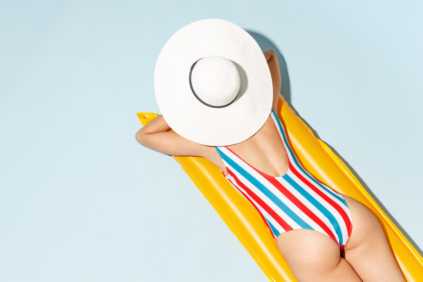 上背部，后视图，年轻性感的女人苗条的身体穿条纹连体泳衣躺在充气床垫上，酒店游泳池孤立在淡蓝色背景。暑假海边休息晒日光浴的概念。图片下载