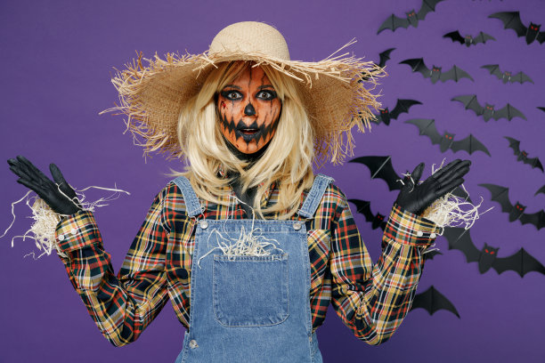 年轻女子带着万圣节化妆面具，戴着草帽稻草人扮相，镜头展开双手孤立在素色深紫色背景下的摄影棚肖像庆祝节日派对概念图片下载