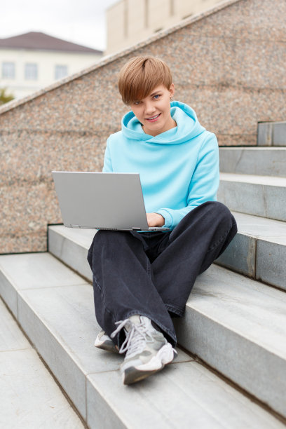 一个年轻的短发女人坐在楼梯上拿着笔记本电脑的垂直照片。在线教育的概念图片下载