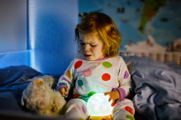 可爱的小女孩在睡觉前玩着五颜六色的夜灯。困倦的女儿穿着睡衣玩得很开心。健康的孩子不睡觉。图片下载