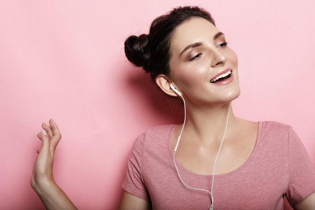 美丽的年轻女子戴着耳机，在粉红色的背景下听音乐图片下载