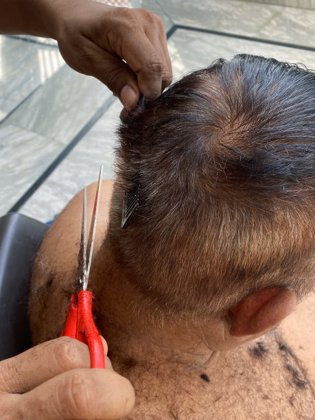 照片中，印度男子赤裸上身，在家理发，理发师用剪子和梳子剪短后背和侧面，后视镜，聚焦前景图片下载