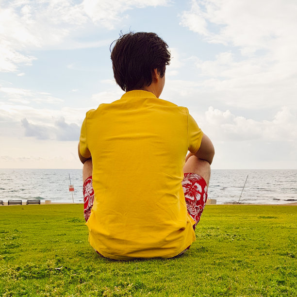 一个年轻人坐在海边眺望远方。他背对着观众坐着。广场的照片,生活方式。图片下载