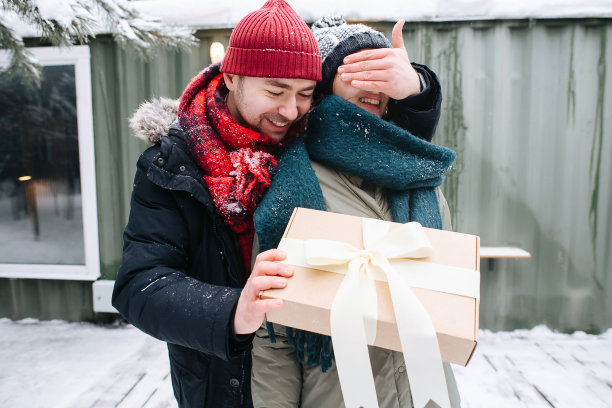 快乐的男人穿着冬衣遮住他女人的眼睛，手里拿着礼物图片下载