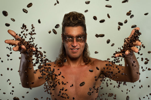脸上皮肤擦洗。性感男模特的肖像应用天然咖啡面膜，面部磨砂面部皮肤。男人的面部真实咖啡面膜和散落的咖啡颗粒通过手指。图片下载