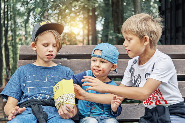 男孩们在公园的长椅上吃着纸袋里的美味爆米花图片下载